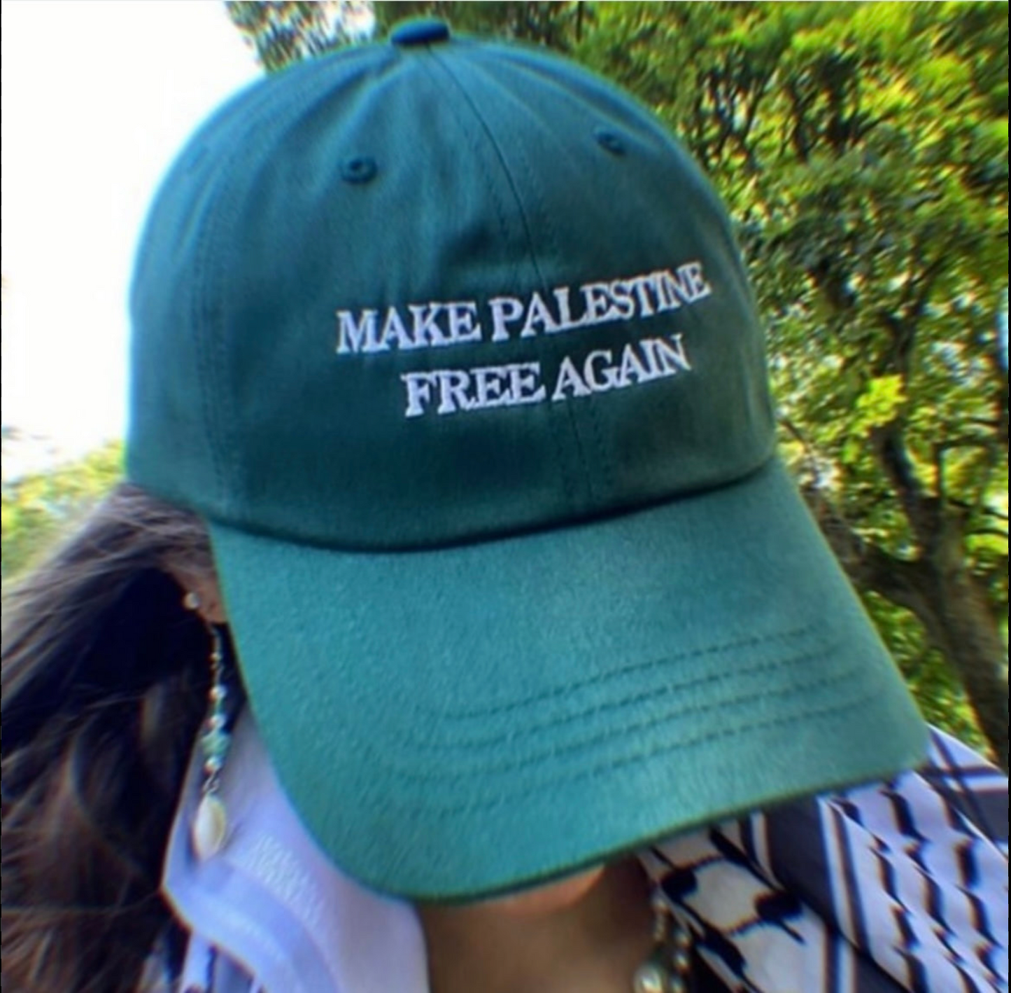 Green cap with 'MAKE PALESTINE FREE AGAIN' text worn by a person outdoors.